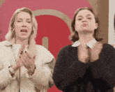 two women are clapping their hands in front of a red letter g