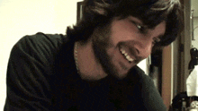 a man with a beard is smiling and wearing a chain around his neck