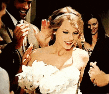 a woman in a wedding dress is holding a bouquet of flowers and waving at her guests .