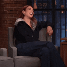 a woman is sitting in a chair laughing with her hands on her knees