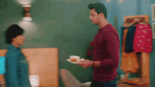 a man in a red shirt is holding a plate of food and a cup of coffee