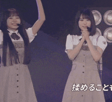 two girls are standing on a stage with their arms in the air and one is holding a microphone ..