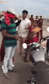 a group of people are standing on a street next to a motorcycle and a man is wearing a red hat .
