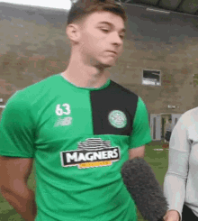 a man in a green shirt is talking into a microphone while standing on a field .