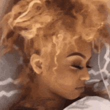 a woman with curly hair is laying in bed with her eyes closed and her hair in a bun .