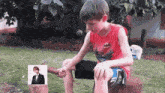 a boy wearing a red batman shirt sits on a stump