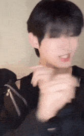 a young man in a black jacket is making a funny face while holding his hands together .