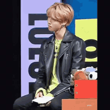 a young man wearing a black leather jacket is sitting on a box with stuffed animals in it