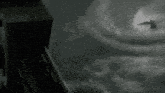 a black and white image of a bird flying through a cloudy sky