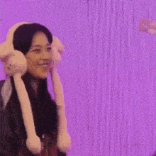 a woman wearing bunny ears and a supreme shirt is smiling in front of a purple screen .