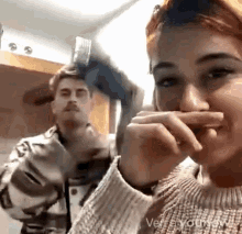 a man and a woman are standing next to each other and the woman is covering her mouth with her hand .