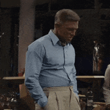 a man in a blue shirt and khaki pants is standing in a room with his hands in his pockets
