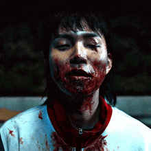 a man with blood on his face is wearing a white shirt and a red necklace