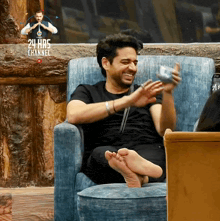 a man sits in a chair with his feet up and a 24 hrs channel advertisement behind him