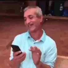 a man in a blue shirt is holding a cell phone in his hand .