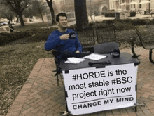 a man sitting at a table with a sign that says change my mind