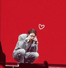 a man is kneeling down on a stage with hearts drawn on the wall behind him .