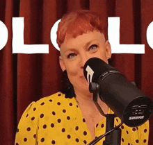 a woman in a yellow and black polka dot shirt is singing into a shure microphone