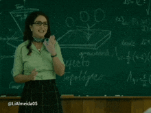 a woman wearing glasses and a scarf is smiling in front of a chalkboard with numbers on it
