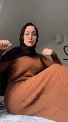 a woman wearing a hijab and a brown dress is sitting on the floor