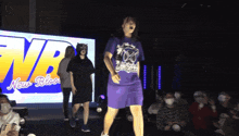 a woman in a purple dress is dancing in front of a large screen that says new blood