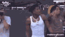 a man in a white tank top is dancing with a group of people .