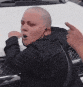 a man with a shaved head is standing in front of a white truck .
