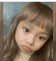 a little girl with long hair and bangs is looking at the camera with a sad look on her face .
