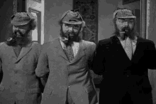 three men with beard and hats are standing next to each other .