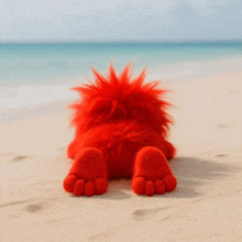 a red stuffed animal is laying on its back on a sandy beach