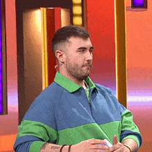 a man wearing a green and blue sweater with a tattoo on his arm