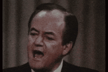a man in a suit and tie is making a funny face while speaking into a microphone .