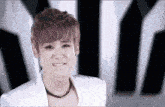 a young man wearing a white jacket and a necklace smiles at the camera