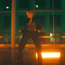 a woman in a black jacket is dancing in front of a building