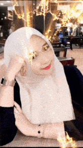 a woman wearing a white hijab and a black shirt is sitting at a table