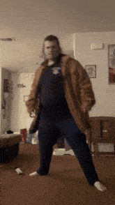a man in a brown jacket and blue pants is dancing in a room