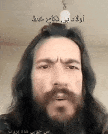 a man with long hair and a beard has a light bulb hanging from the ceiling above him