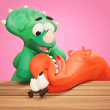 a cartoon of a green dinosaur and an orange worm on a wooden table