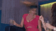 a woman in a pink dress is holding a drink in her hand and giving the middle finger .