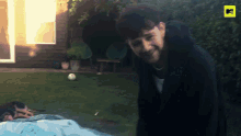 a man in a black jacket stands in a backyard with a yellow mtv logo in the corner