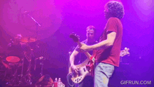a man in a red shirt is playing a guitar in front of a purple background with gifrun.com in the corner