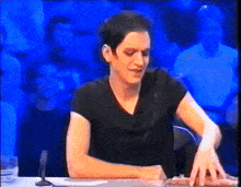 a man in a black shirt is sitting at a table in front of a microphone