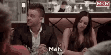 a man and a woman are sitting at a table in a restaurant and the man is saying meh .
