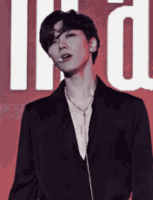 a man in a black jacket and necklace is standing in front of a red background .
