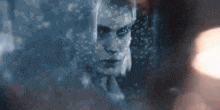 a woman 's face is reflected in a window with rain drops on it