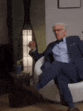 a man in a suit and bow tie is sitting on a chair with his legs crossed .