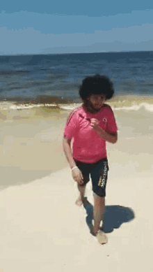 a man in a pink shirt and black shorts is walking on the beach