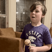 a young boy wearing a purple k-state shirt is holding a toy