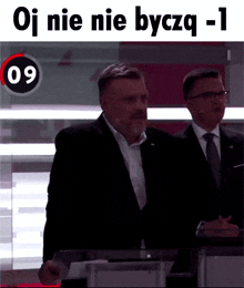 a man in a suit and tie stands in front of a sign that says oj nie nie byczq -1
