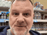 a man with a beard is making a funny face in front of a shelf of soda bottles .